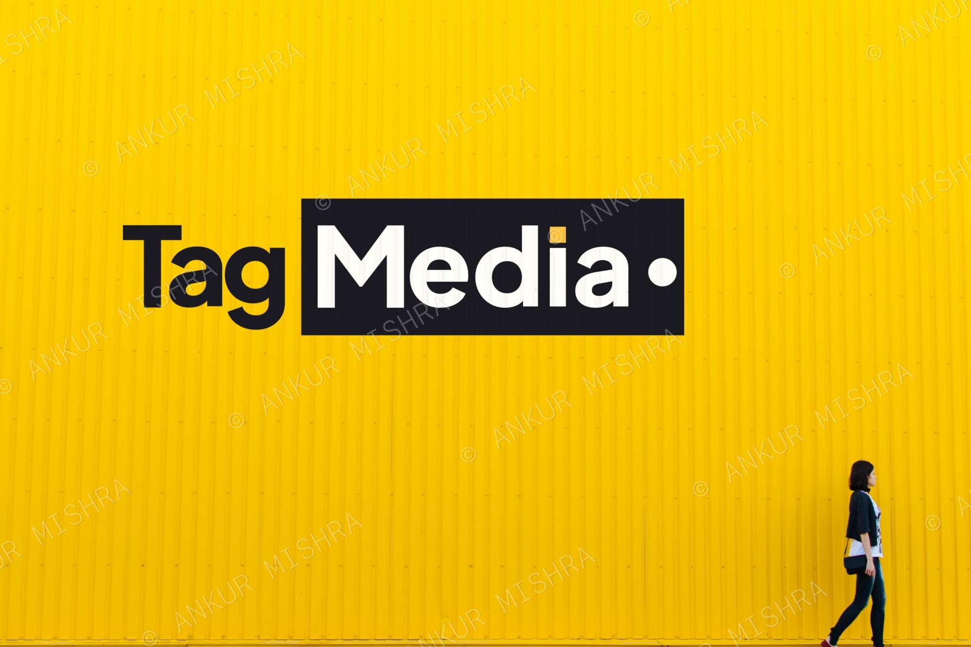 Tag Media wordmark painted on a yellow corrugated wall with a passerby